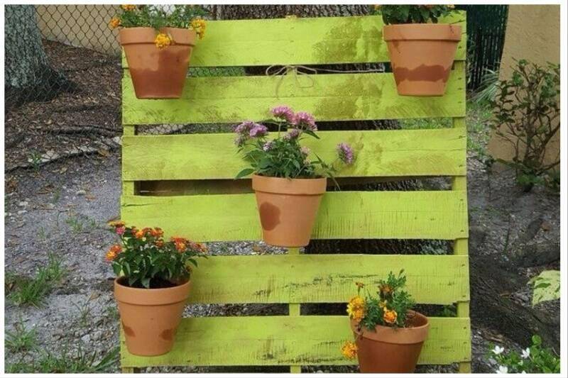 Wooden pallet painted green with pots hanging on it.