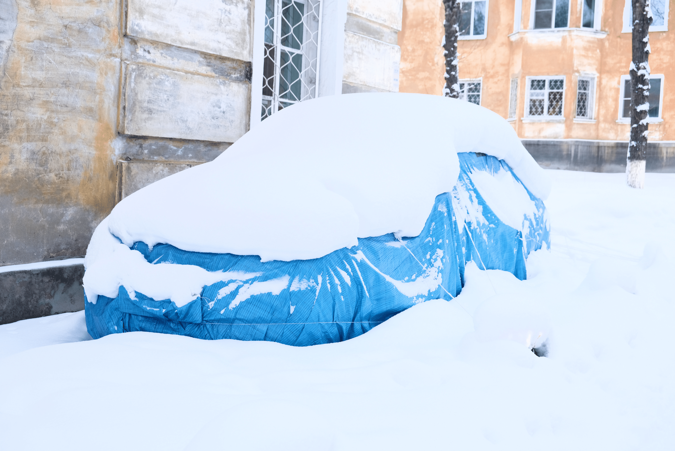 Car under a blue tarp covered in snow.