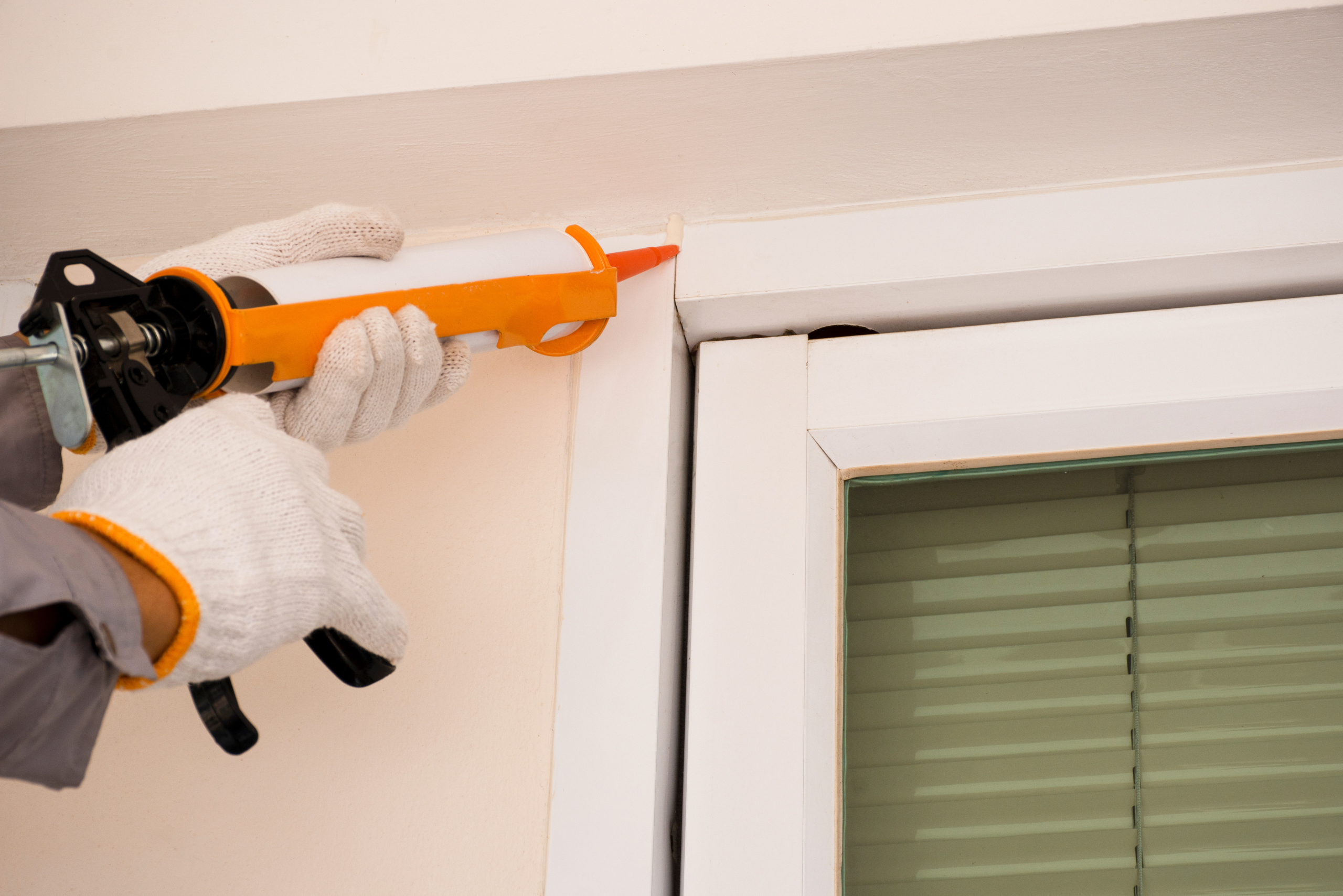 Person applying caulking to a window from the outside.