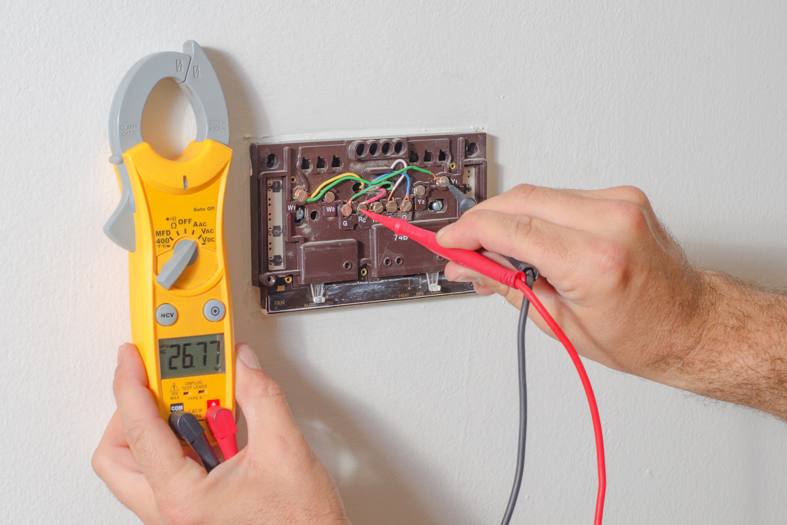 Using a voltage tester to check power for a thermostat connection.