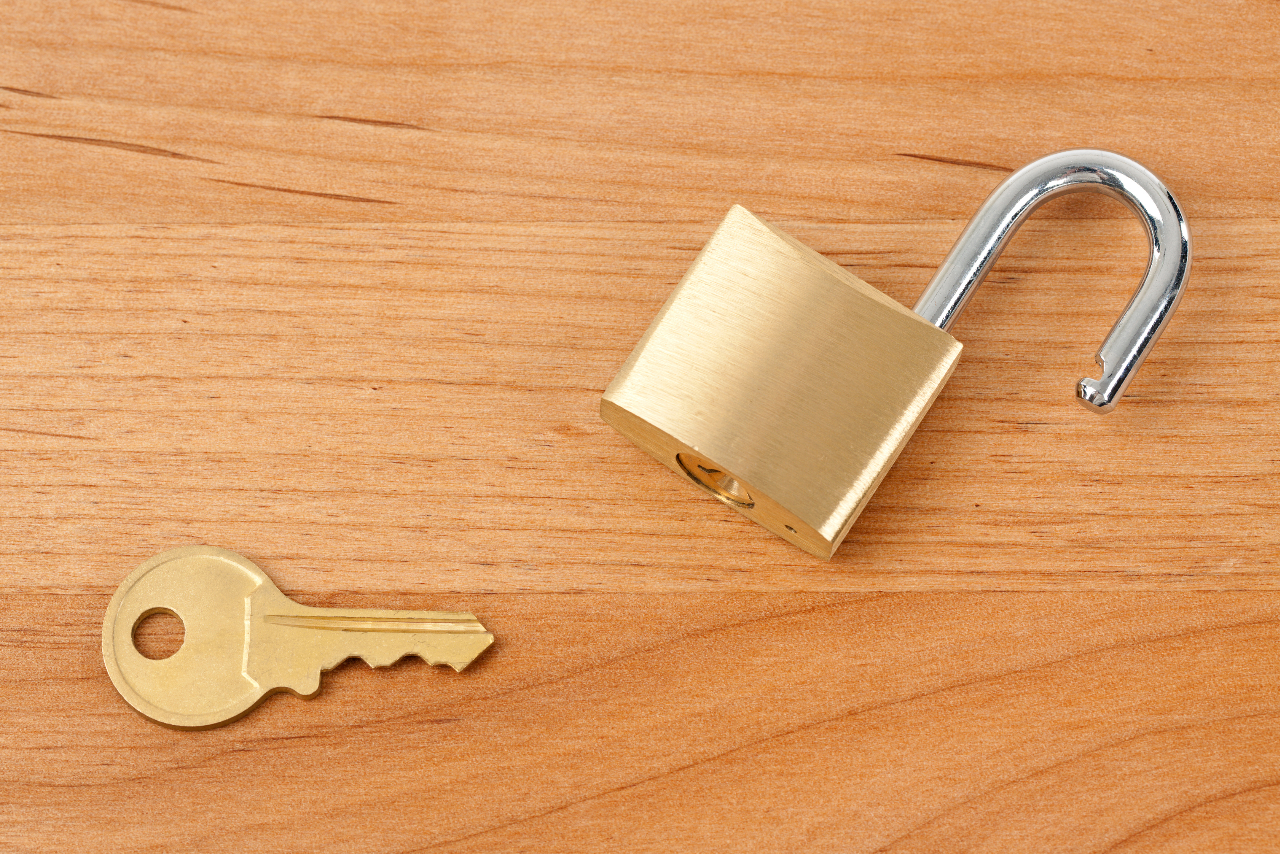 A key and padlock on wooden surface.