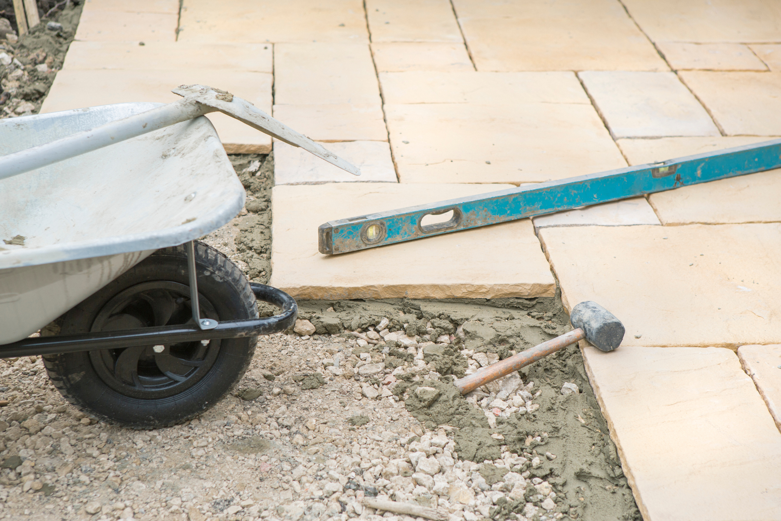 Wheelbarrow, mallet, and level at a patio stone installation in a backyard.