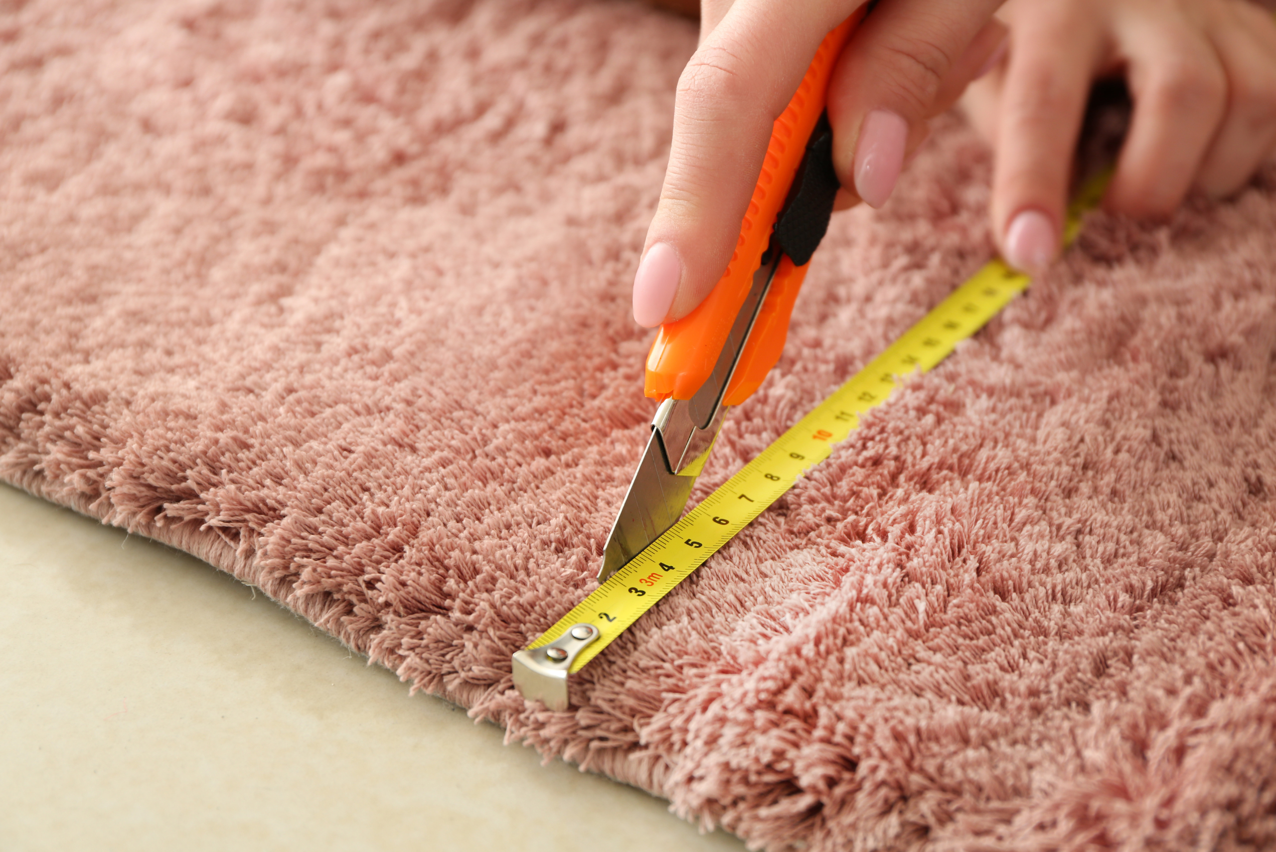 Cutting a pink carpet using utility knife.