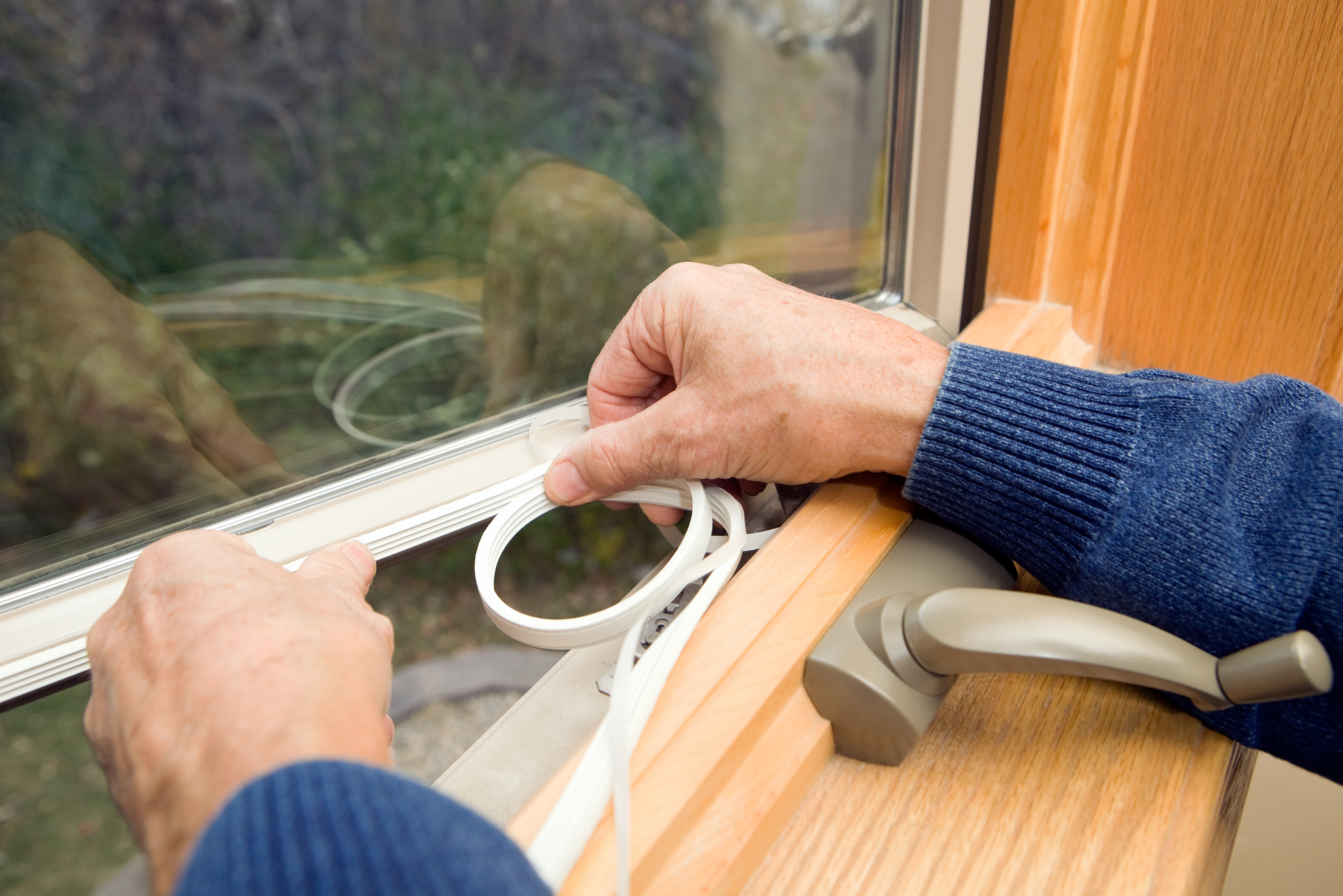 Closeup of someone's hands installing a window seal to an open window.