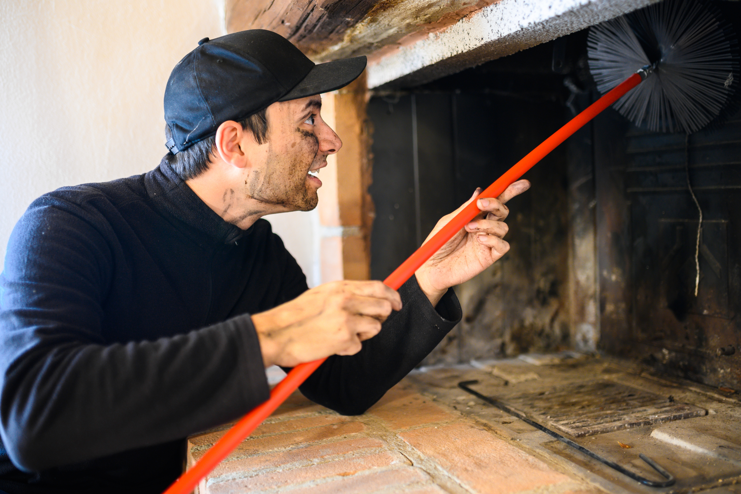 Worker using a brush to clean out fireplace chimney.