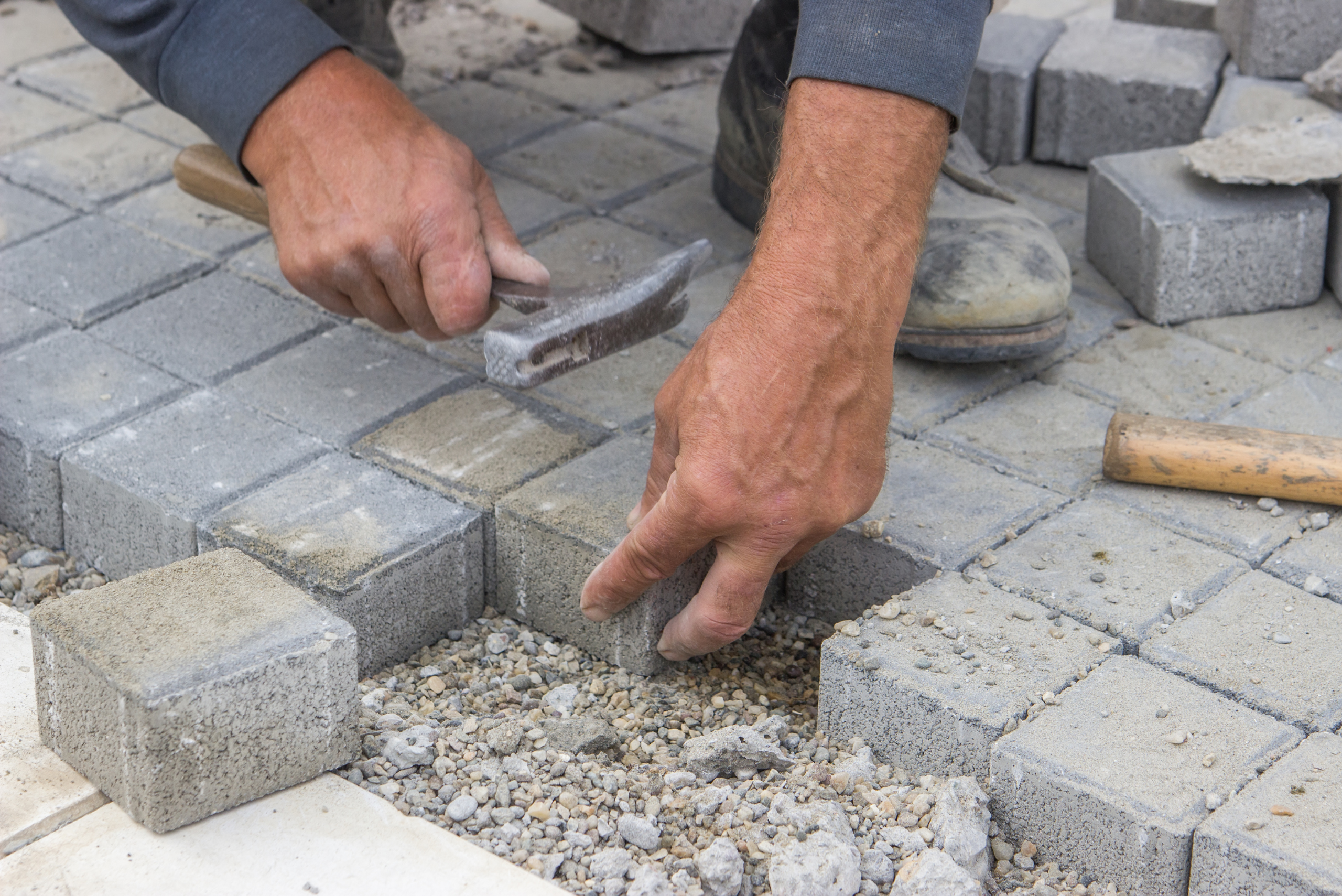 Man installing concrete pavers using a hammer.