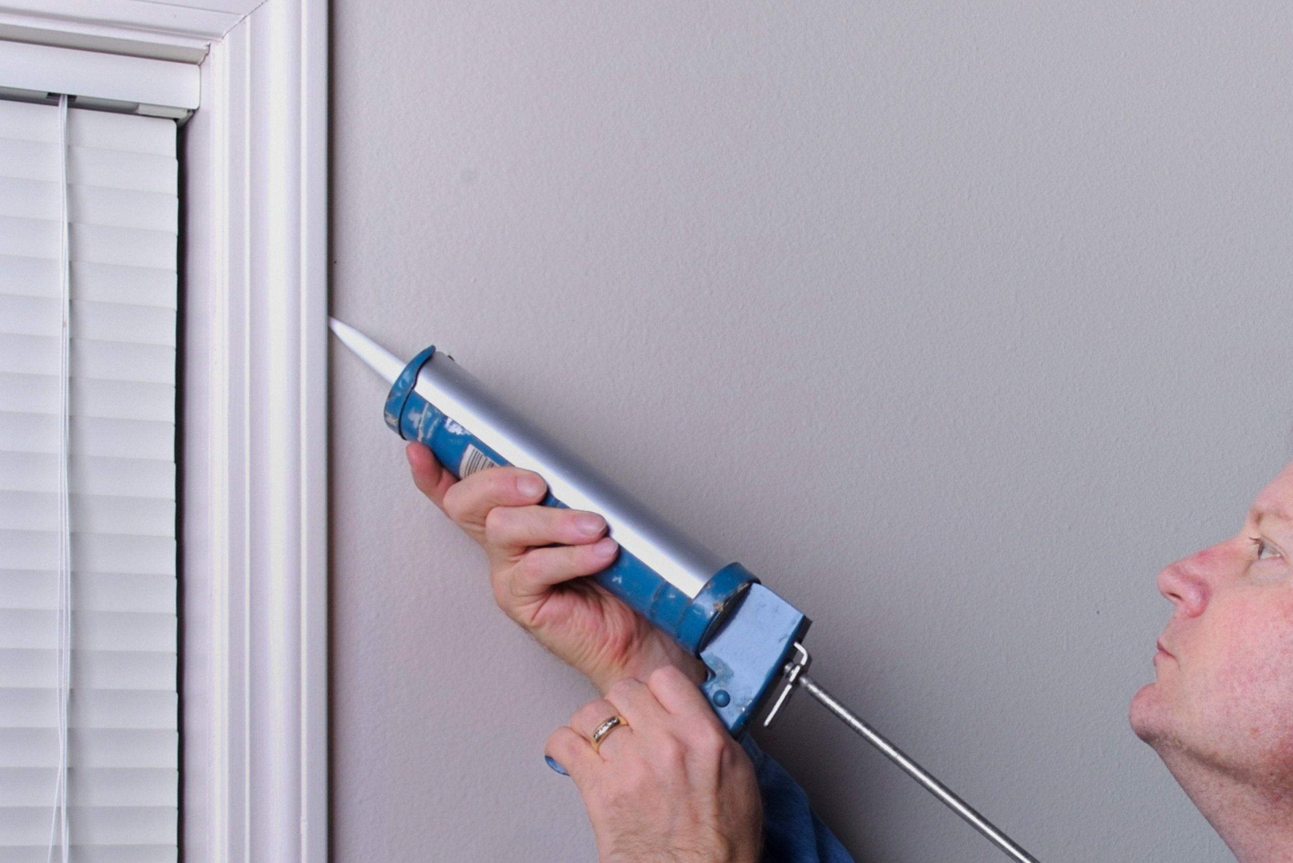 Person applying caulking to a frame of a window.