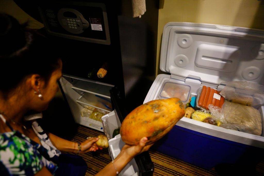 Woman moving things around a cooler and fridge.