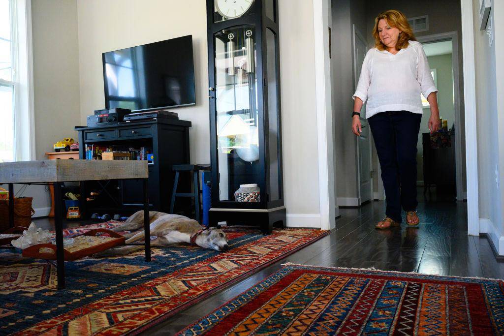 Dog sitting on the floor of a room as a woman enters from the door.