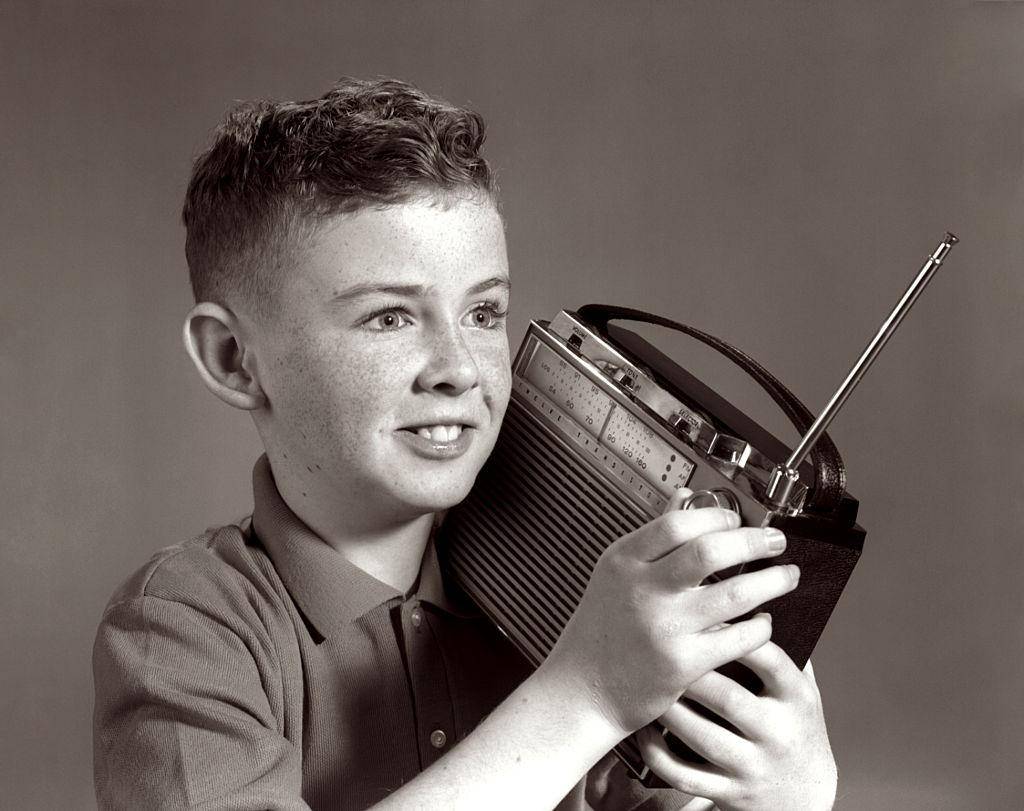 Black and white photo of a child holding a radio on their shoulder.