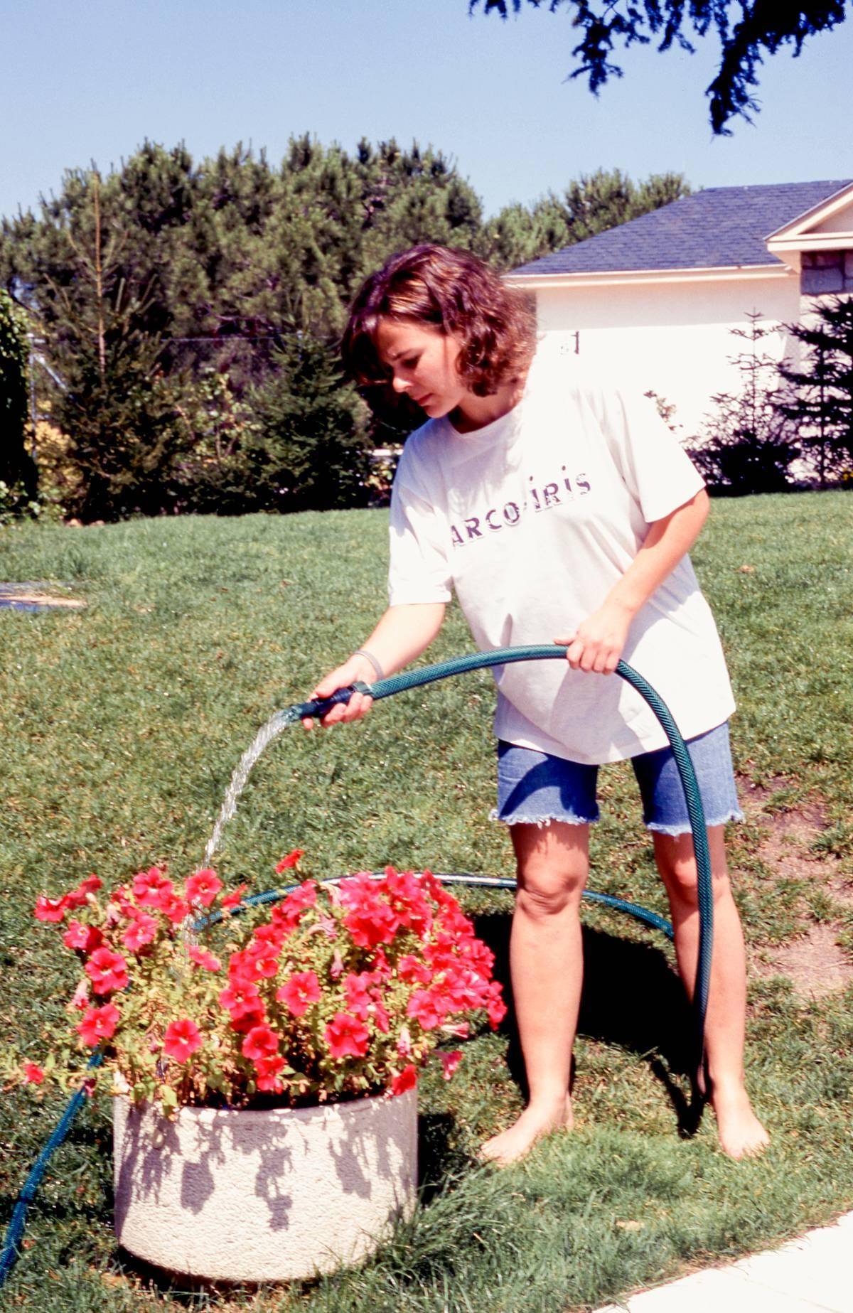 Woman watering pot of flowers.