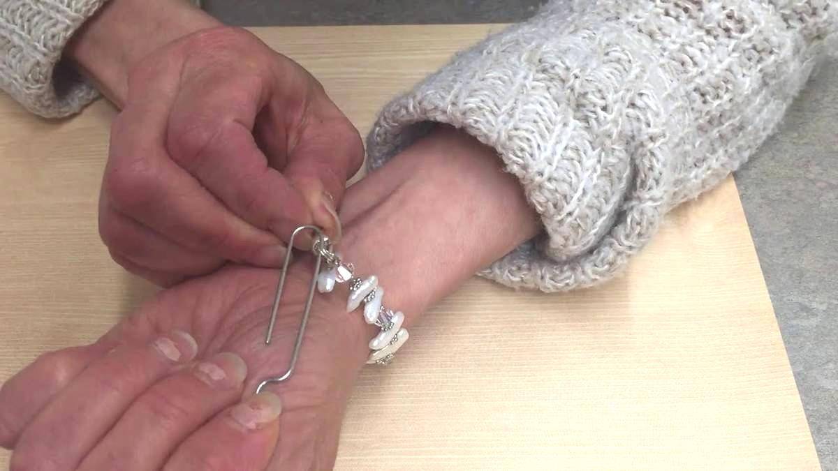 Woman using a clip to put on a bracelet. 