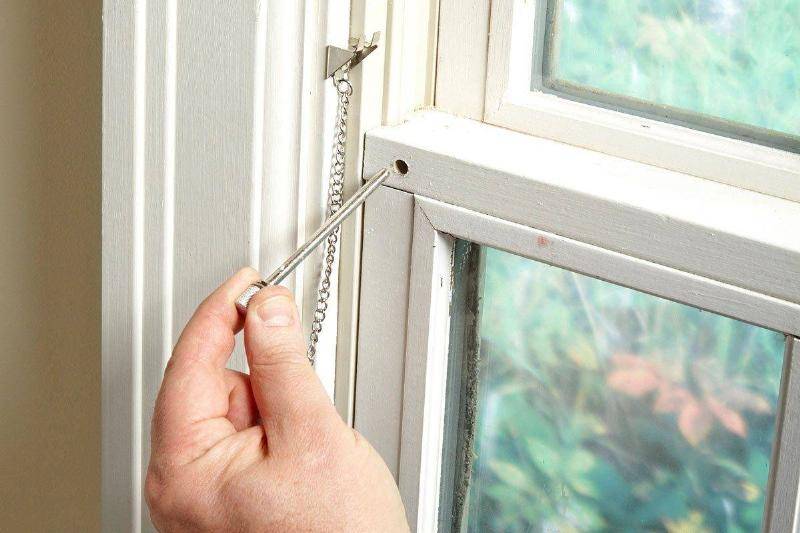 A person inserts a pin lock into a window.