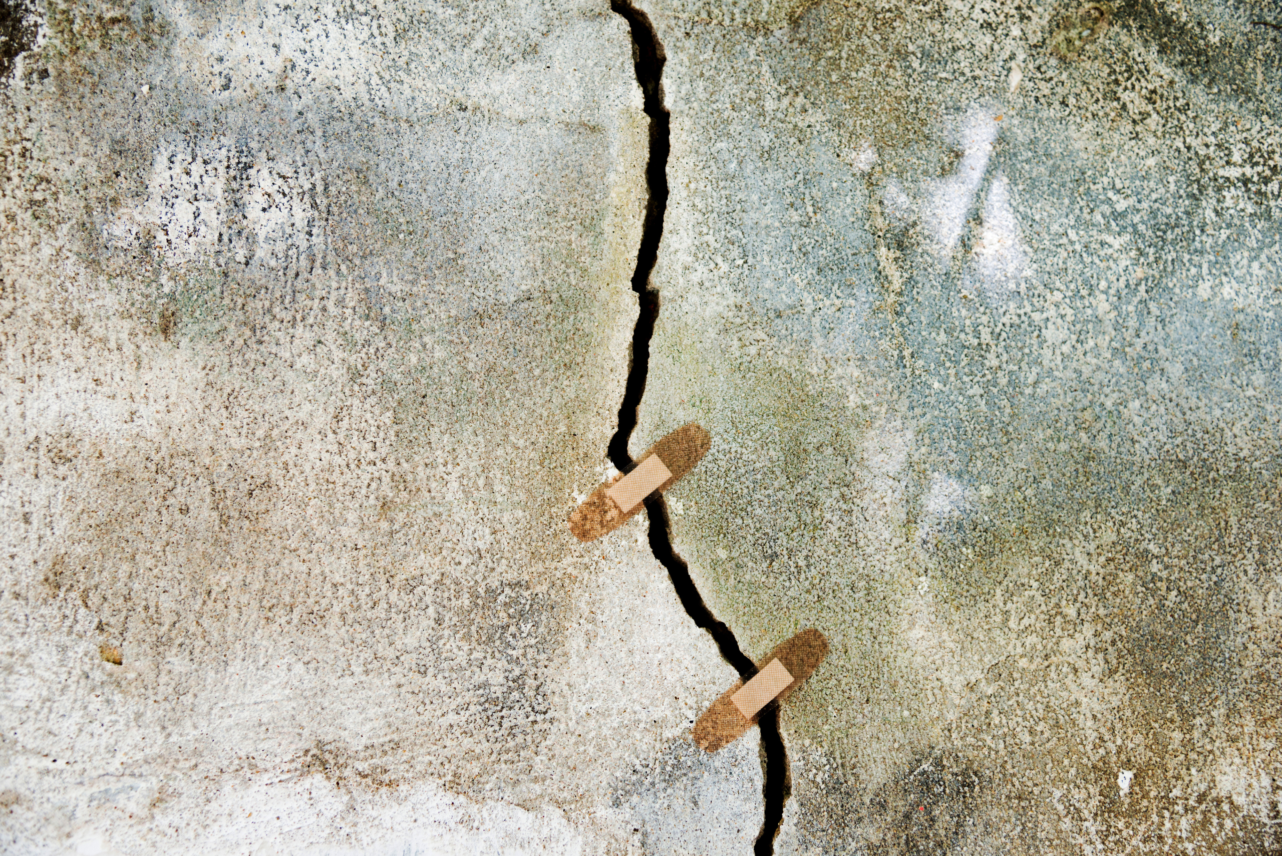 Cracked concrete driveway with band-aids on the crack.