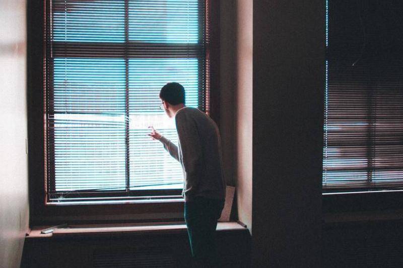 A man peeks outside of the window by moving the blinds.