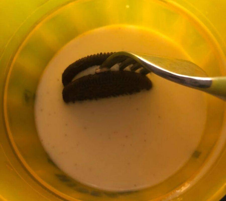 a fork stuck into the middle of an oreo cookie being dipped in milk