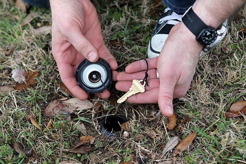 A person takes a spare key out of a fake sprinkler.