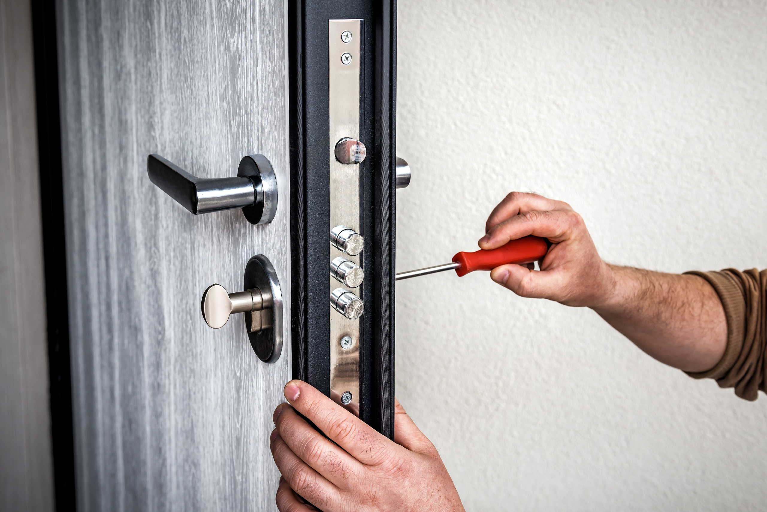 Close up of someone's hands using a screwdriver on a door lock.