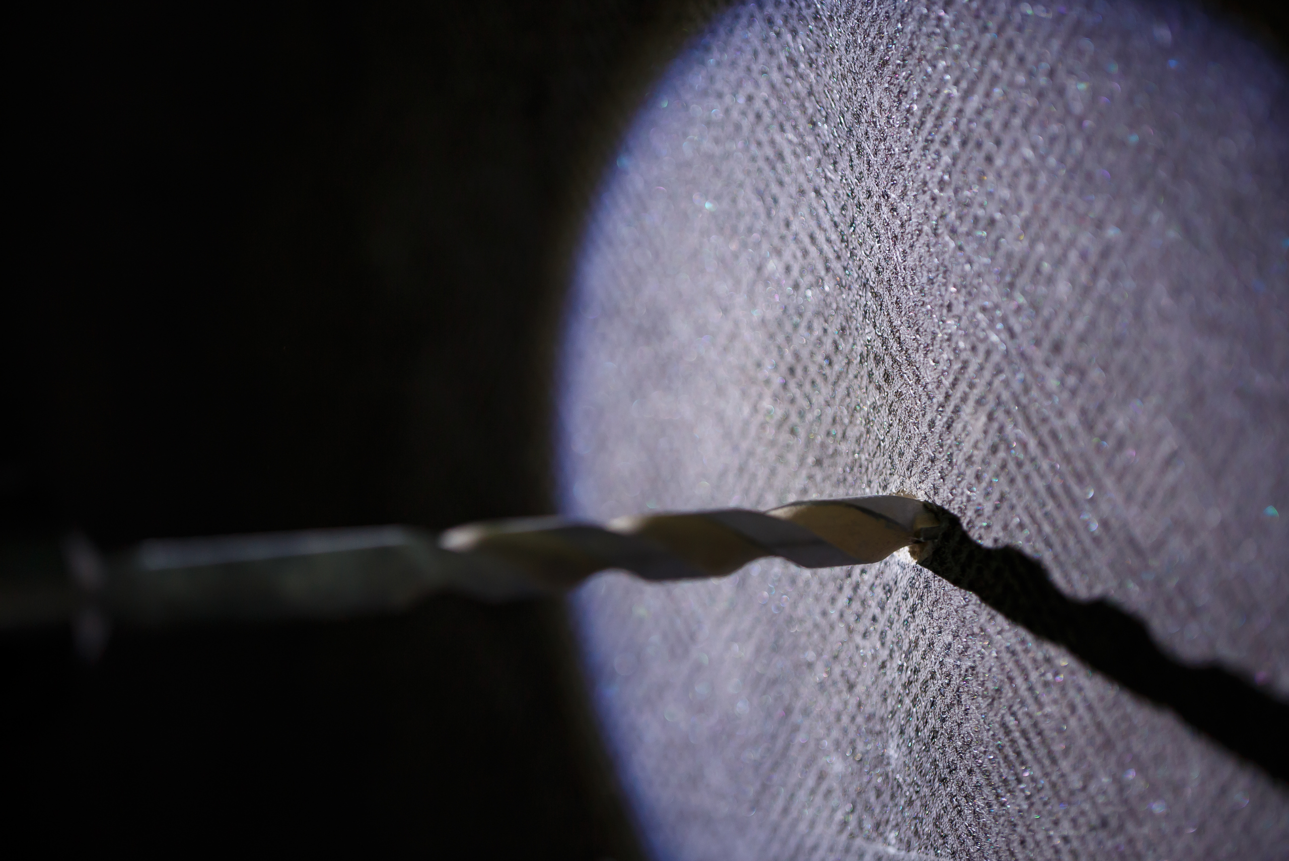 Drill bit against a concrete wall with light on.