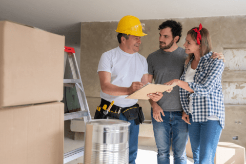 Couple talking to a contractor wearing a yellow safety helmet.