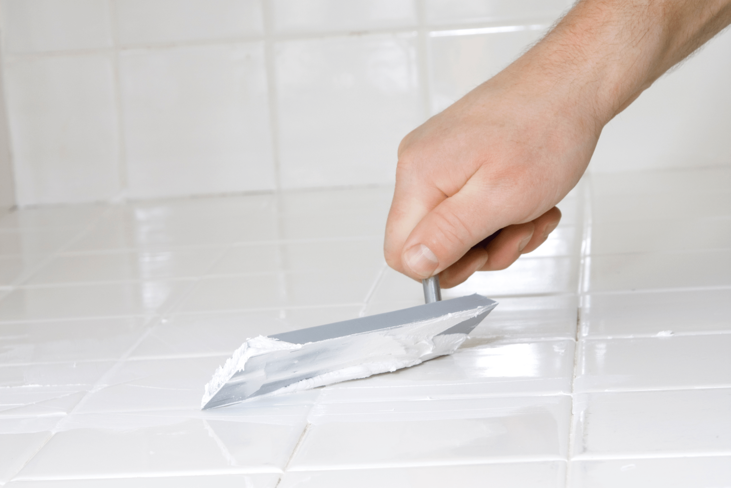 Spreading new grout using a tool on bathroom tile.