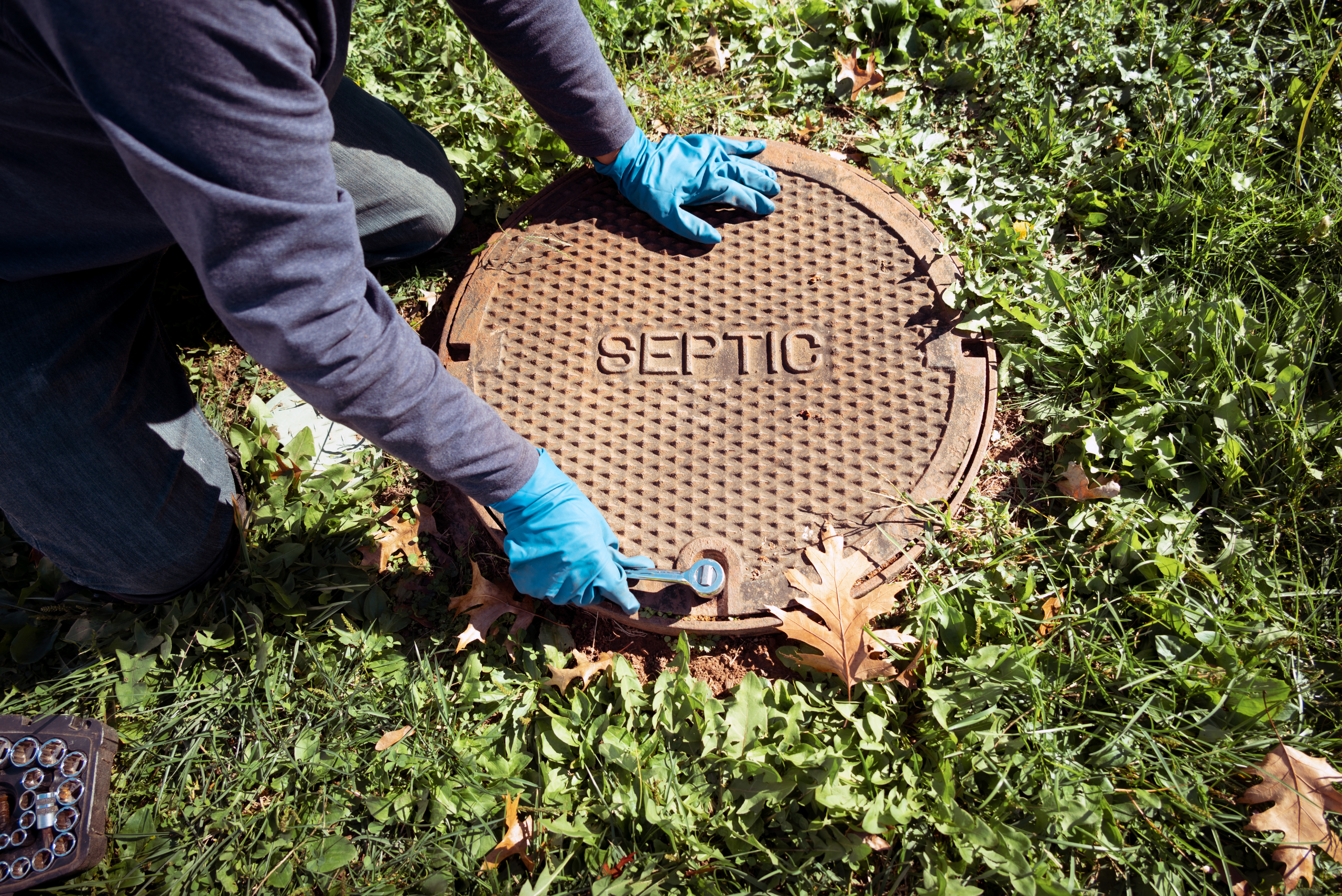 Unbolting a metal septic tank cover.