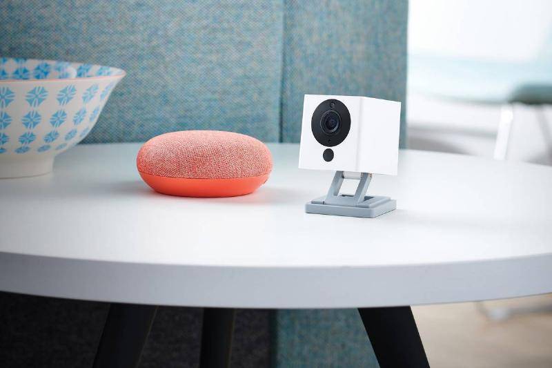 A Neos SmartCam home security camera stands on a coffee table.