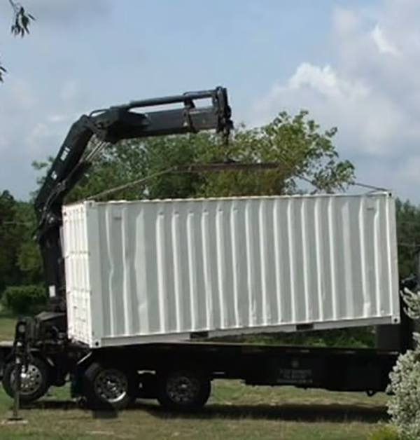 Crane pulling a white container off a trailer.