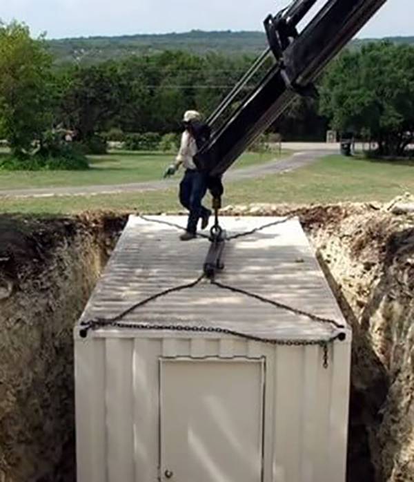 Crane lowering white container into the ground.