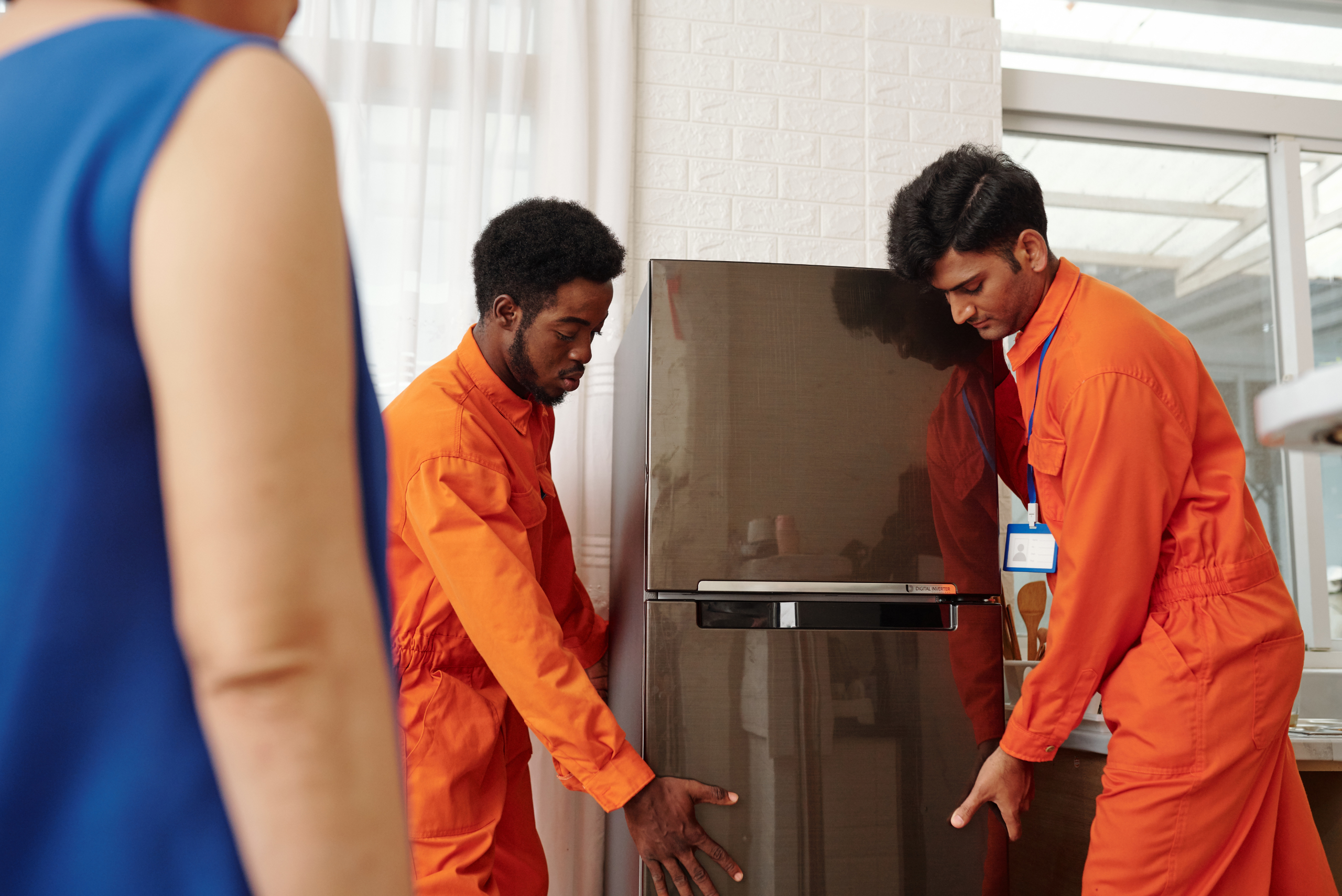 Two men in orange outfits moving a fridge.