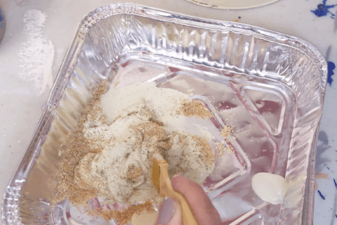 Mixing sand and paint in an aluminum pan.