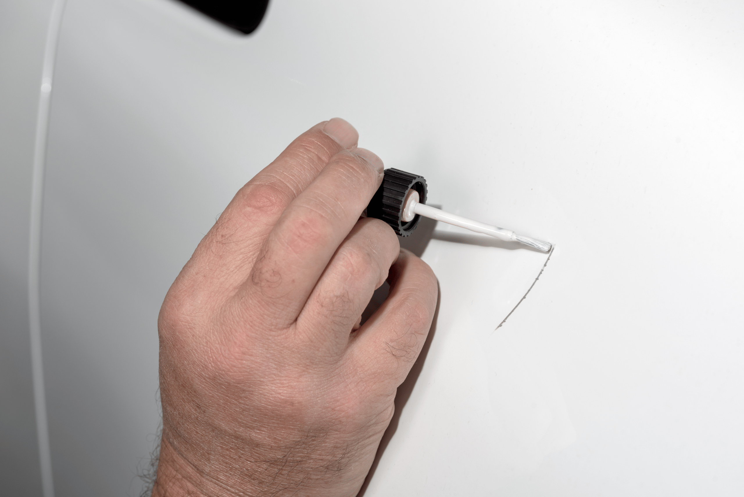 Closeup of someone's hand applying touch up paint to a white car.