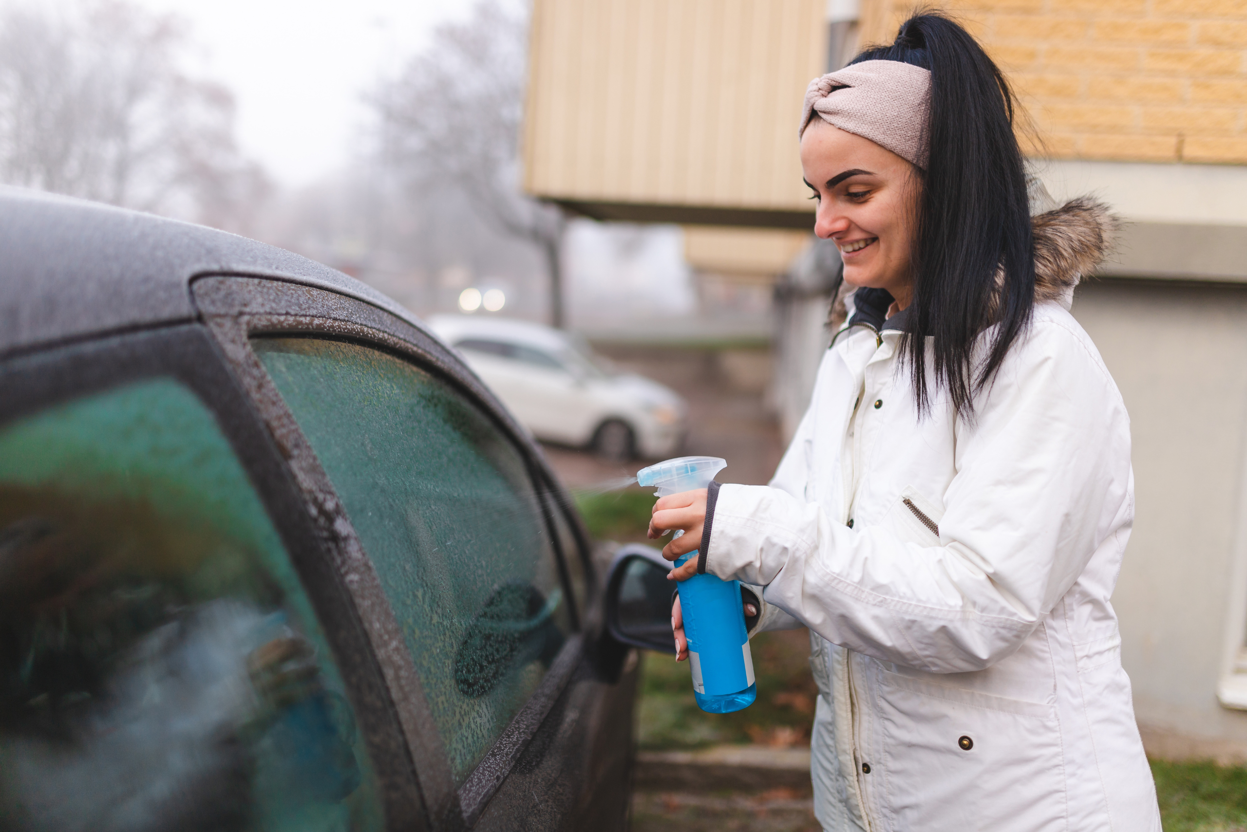 Girl spraying the side window of a car with blue defrosting liquid.