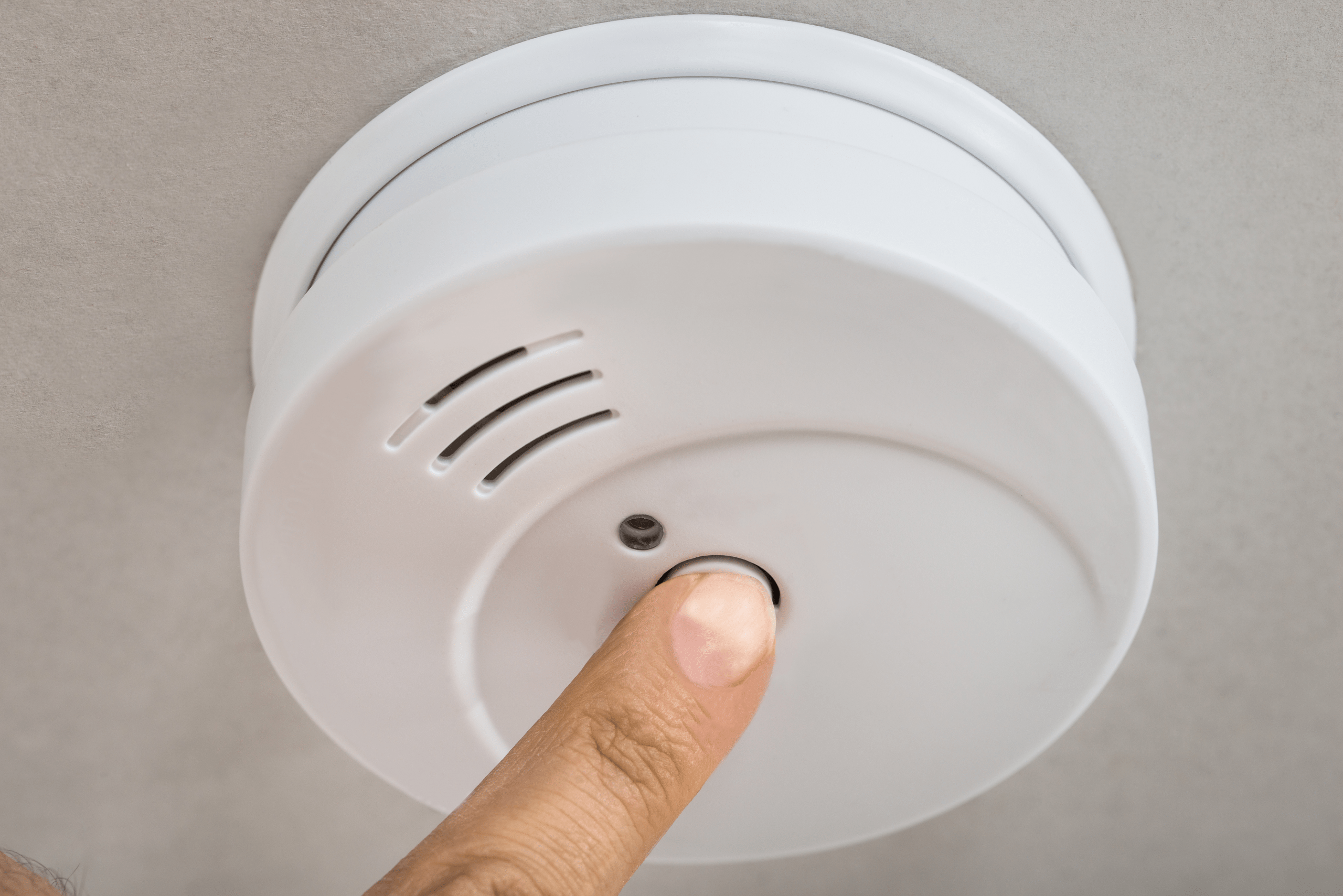 Closeup of someone's finger pressing the fire detector test button.