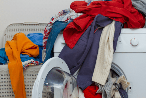 Messy clothes all over a washing machine.