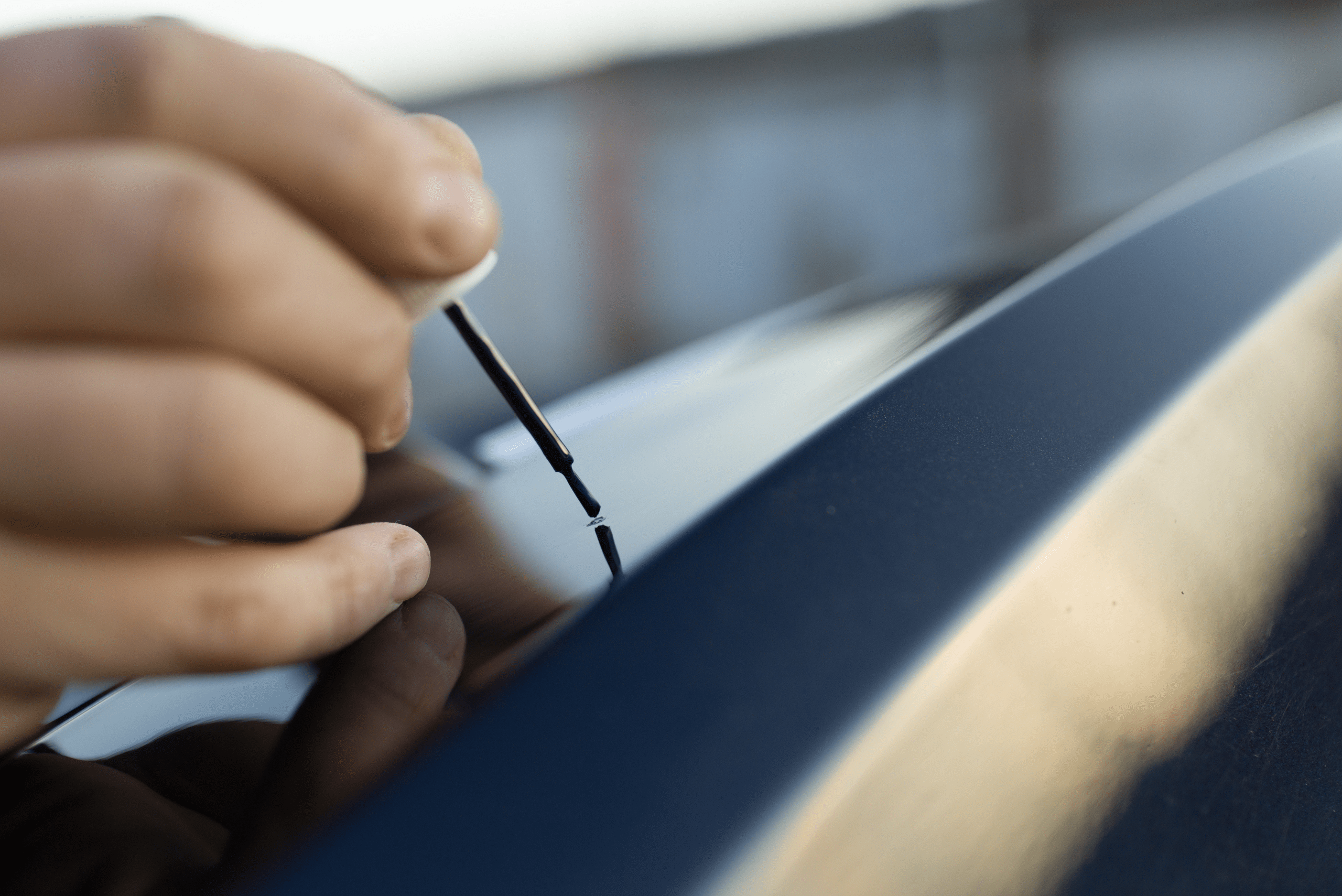 Closeup of someone's hand applying touch up paint to a blue car.