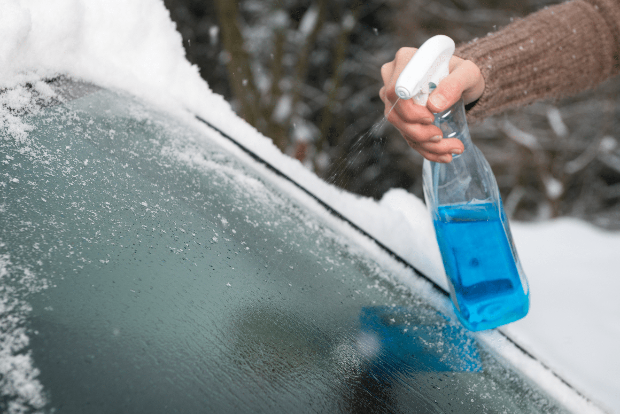 Closeup of someone's hand using a spray bottle to put blue liquid on windshield of a car.