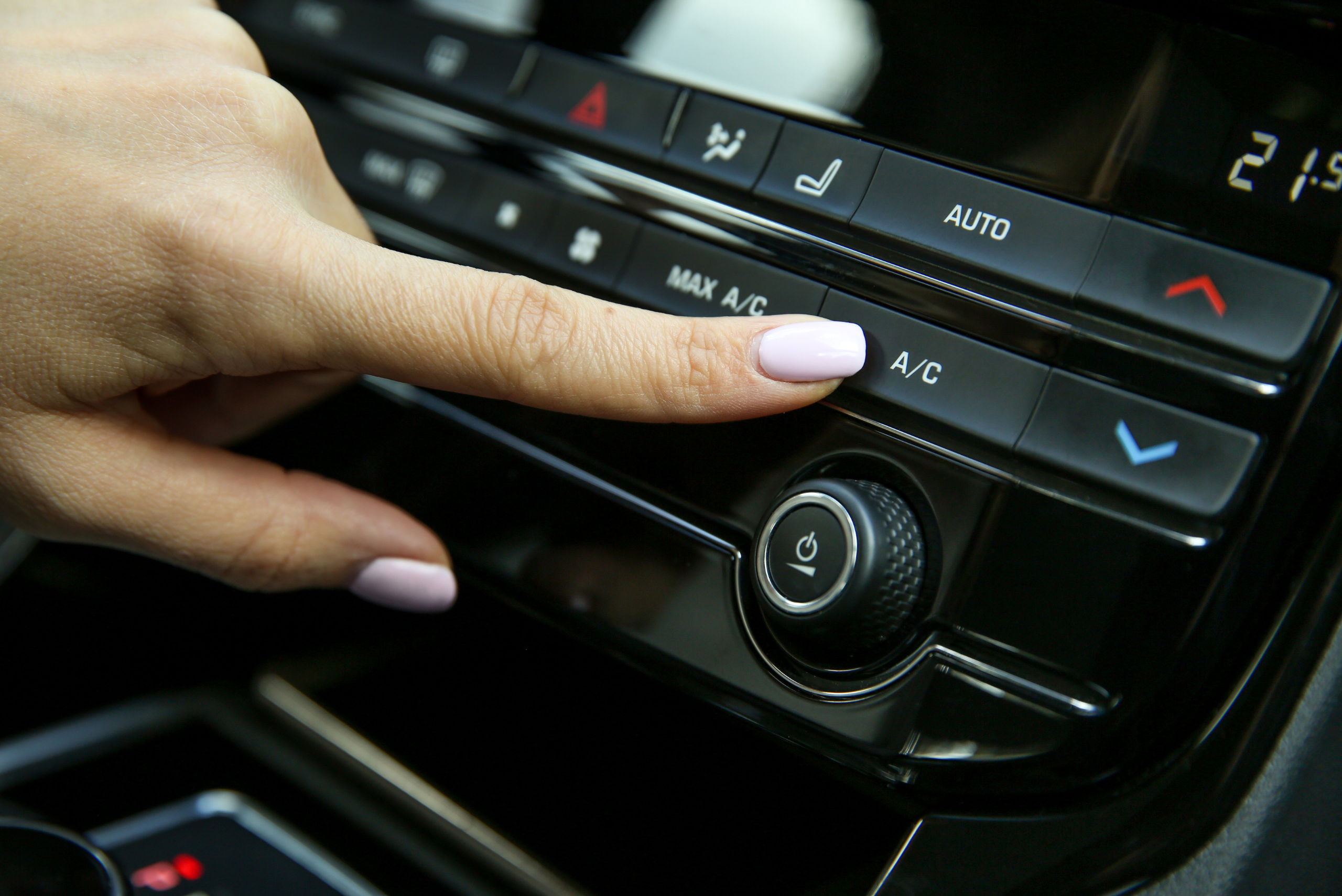 Closeup of someone's hand pressing the A/C button inside a car.