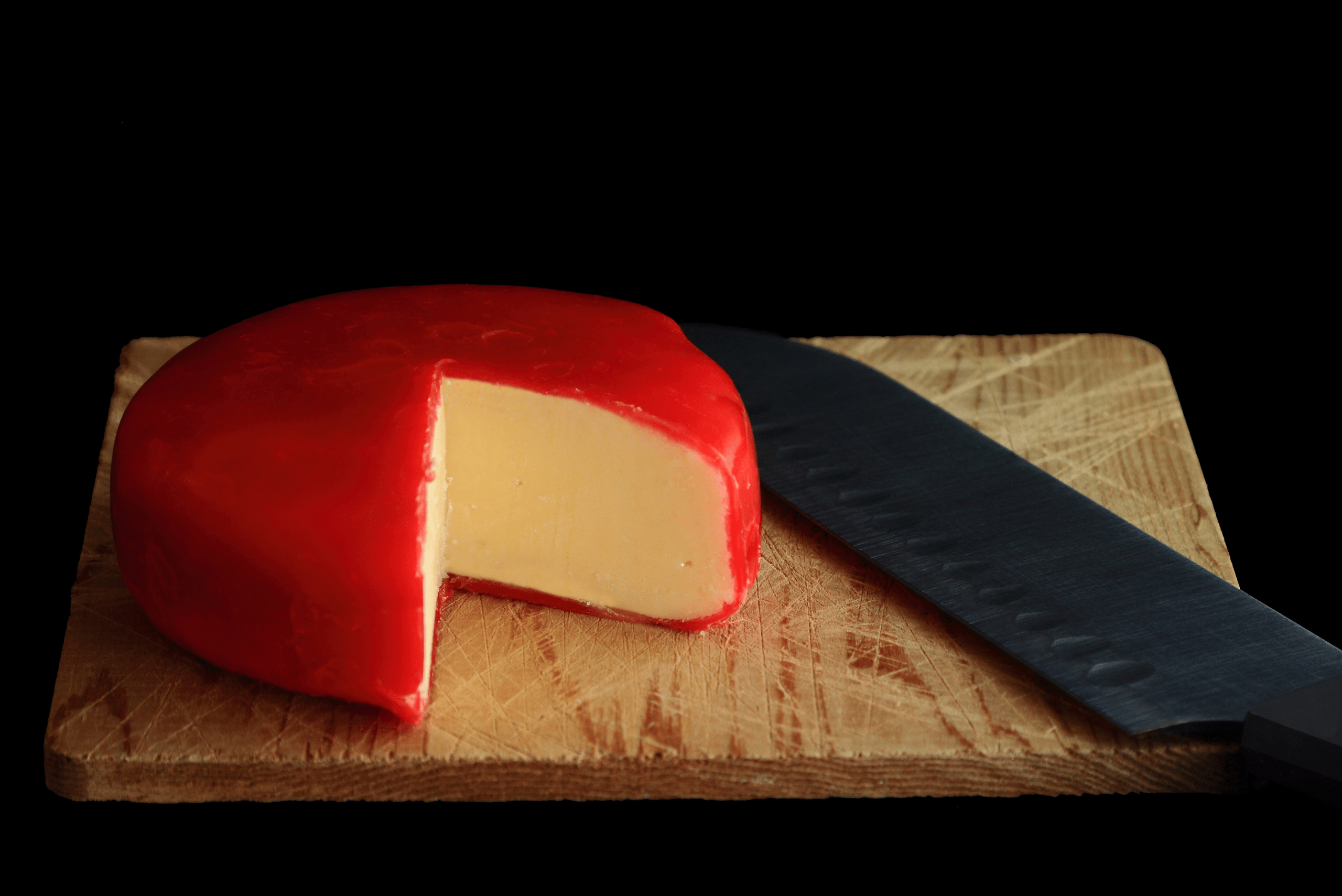 Block of Gouda cheese covered in red plastic and cut.