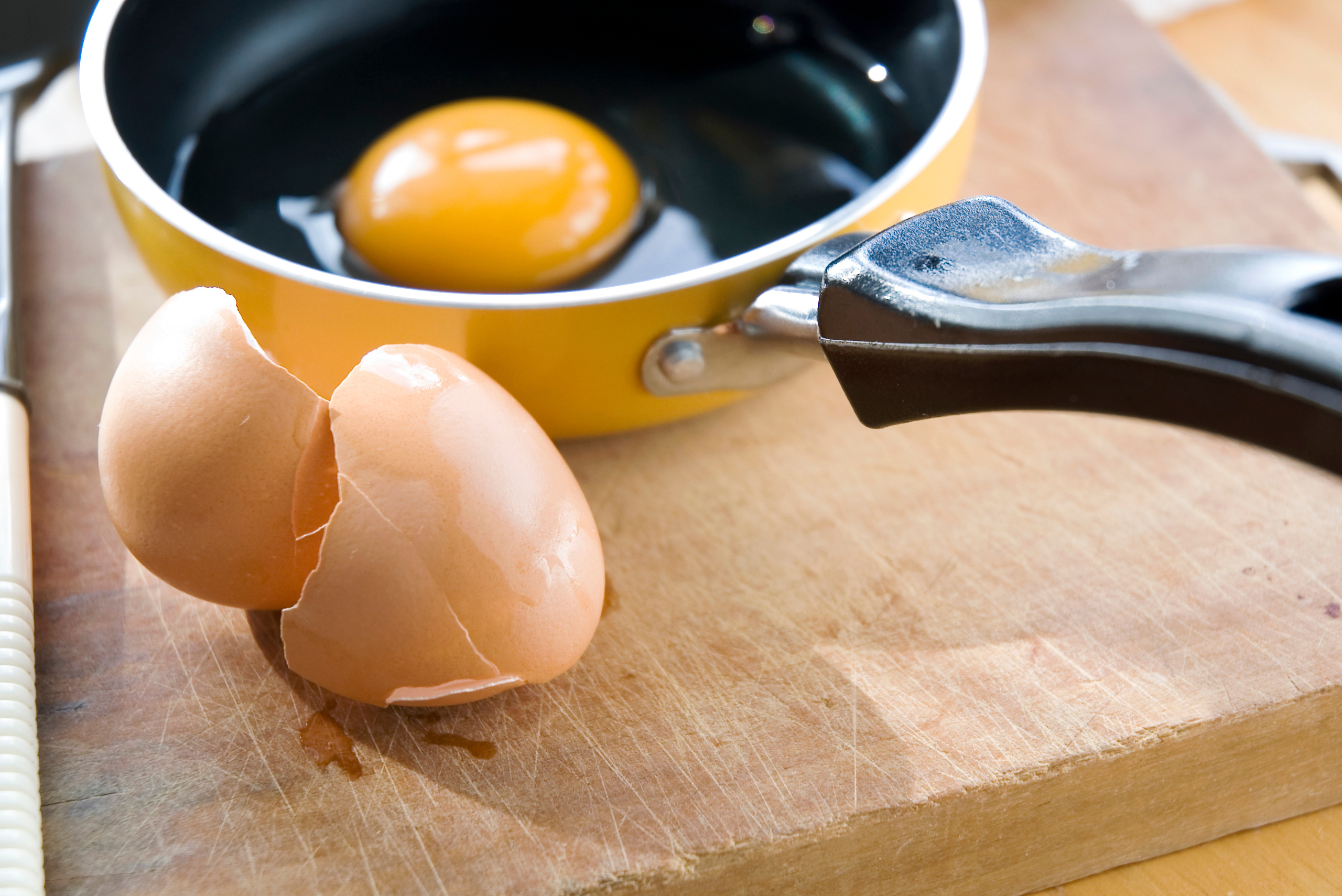 Eggs in a pan and eggshells on the wooden countertop.