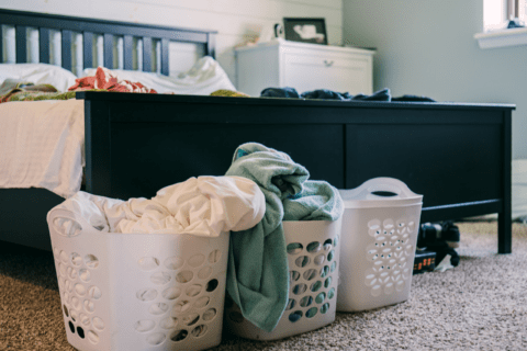 Three laundry baskets in front of a bed.