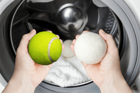 Two hands in front of dryer, one holding a tennis ball, the other a dryer ball.