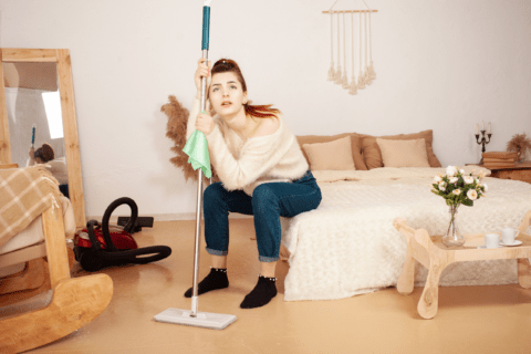 Tired woman leaning on a mop as she sits on the edge of a coach.