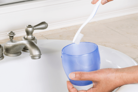 Cleaning tooth brush in sink.