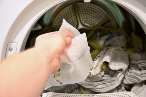 Person's hand adding dryer sheet to dryer.