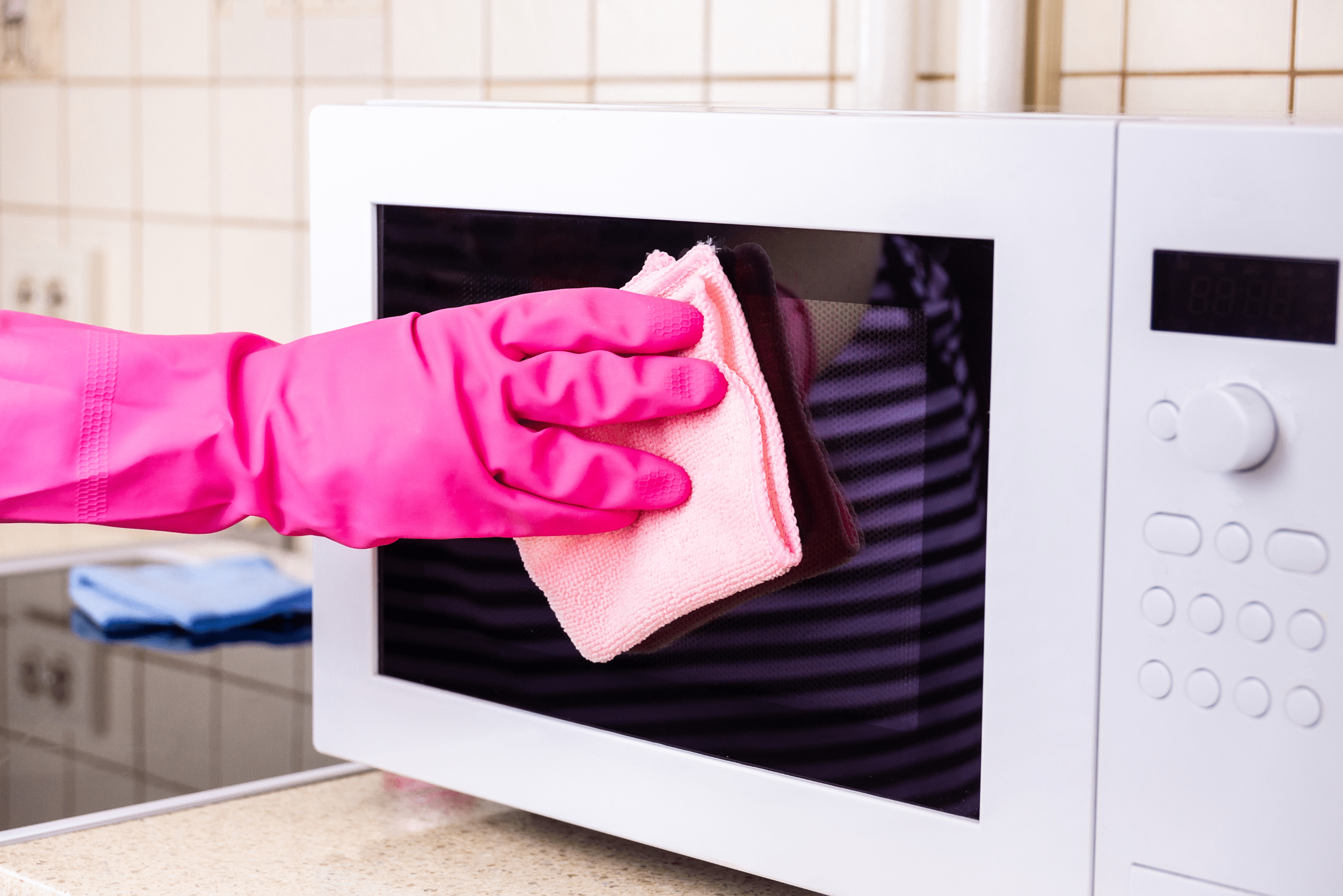 Hand wearing pink gloves using a pink microfiber to clean microwave.