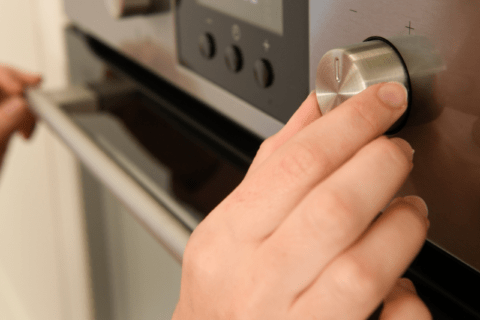 Closeup of someone's hand adjusting oven knob.