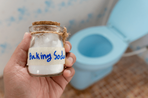 Holding baking soda glass jar in front of blue toilet.